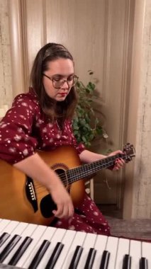 Şık elbiseli ve gözlüklü güzel bir genç kadın evde çalışırken gitar çalar. İçeride yaratıcılığın ve adanmışlığın huzurlu bir anı. Hobi ve boş zaman