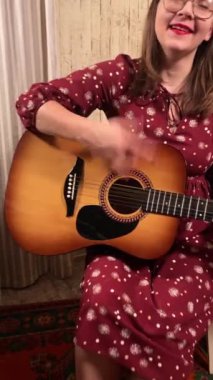 Şık elbiseli ve gözlüklü güzel bir genç kadın evde çalışırken gitar çalar. İçeride yaratıcılığın ve adanmışlığın huzurlu bir anı. Hobi ve boş zaman
