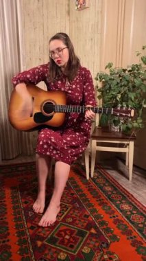 Şık elbiseli ve gözlüklü güzel bir genç kadın evde çalışırken gitar çalar. İçeride yaratıcılığın ve adanmışlığın huzurlu bir anı. Hobi ve boş zaman