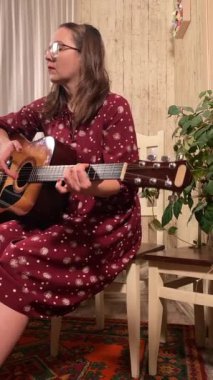 Şık elbiseli ve gözlüklü güzel bir genç kadın evde çalışırken gitar çalar. İçeride yaratıcılığın ve adanmışlığın huzurlu bir anı. Hobi ve boş zaman