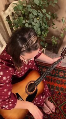 Şık elbiseli ve gözlüklü güzel bir genç kadın evde çalışırken gitar çalar. İçeride yaratıcılığın ve adanmışlığın huzurlu bir anı. Hobi ve boş zaman