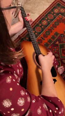 Şık elbiseli ve gözlüklü güzel bir genç kadın evde çalışırken gitar çalar. İçeride yaratıcılığın ve adanmışlığın huzurlu bir anı. Hobi ve boş zaman
