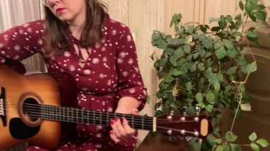 Şık elbiseli ve gözlüklü güzel bir genç kadın evde çalışırken gitar çalar. İçeride yaratıcılığın ve adanmışlığın huzurlu bir anı. Hobi ve boş zaman