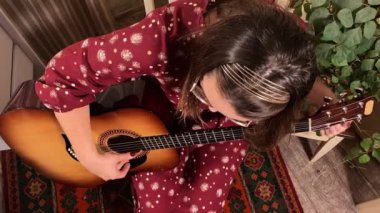 Şık elbiseli ve gözlüklü güzel bir genç kadın evde çalışırken gitar çalar. İçeride yaratıcılığın ve adanmışlığın huzurlu bir anı. Hobi ve boş zaman