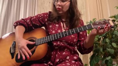 Şık elbiseli ve gözlüklü güzel bir genç kadın evde çalışırken gitar çalar. İçeride yaratıcılığın ve adanmışlığın huzurlu bir anı. Hobi ve boş zaman