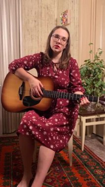 Şık elbiseli ve gözlüklü güzel bir genç kadın evde çalışırken gitar çalar. İçeride yaratıcılığın ve adanmışlığın huzurlu bir anı. Hobi ve boş zaman