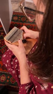Şık elbiseli ve gözlüklü güzel bir genç kadın evde çalışırken kalimba çalar. İçeride yaratıcılığın ve adanmışlığın huzurlu bir anı. Hobi ve boş zaman