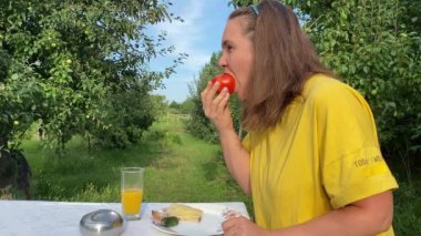 Güzel genç bir kadın ağaçlarla çevrili yemyeşil bir parkta gündelik bir öğle yemeğinin tadını çıkarıyor. Rahatlayarak ve yemeğin tadını çıkararak, temiz hava ve doğada biraz dinlenir..