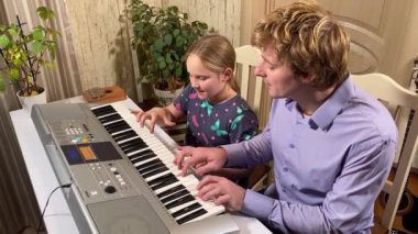 A young music teacher guides a child in learning to play the digital piano Indoors. They focus on mastering the basics of music, fostering creativity and skill development in a supportive environment