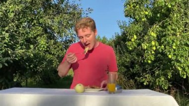 Genç bir adam ağaçlarla çevrili yemyeşil bir parkta gündelik bir öğle yemeğinin tadını çıkarıyor. Rahatlayarak ve yemeğin tadını çıkararak, temiz hava ve doğada biraz dinlenir.