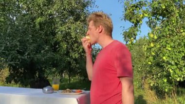 Genç bir adam ağaçlarla çevrili yemyeşil bir parkta gündelik bir öğle yemeğinin tadını çıkarıyor. Rahatlayarak ve yemeğin tadını çıkararak, temiz hava ve doğada biraz dinlenir.