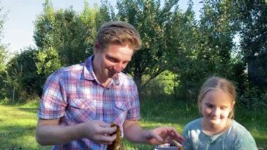 Genç bir baba ve kızı arka bahçede evcil kemirgenlerle ilgilenerek birlikte kaliteli vakit geçirmenin keyfini çıkarıyorlar. Aile ve çocuk, küçük hayvanlarına sevgi dolu bir şekilde açık hava ortamında bakıyorlar.