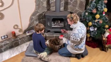 Genç bir baba ve çocuk, şöminenin başında rahat vakit geçirmenin keyfini çıkarırlar. Kış zamanının sıcaklığını ve konforunu kucaklarlar. Hygge konsepti. Aile bağları ve birlikte değerli anları paylaşıyorlar.