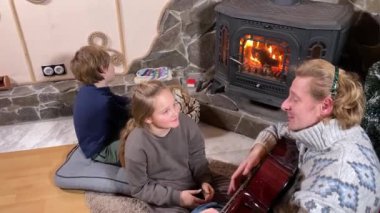 Genç bir baba ve çocuk, şöminenin başında rahat vakit geçirmenin keyfini çıkarırlar. Kış zamanının sıcaklığını ve konforunu kucaklarlar. Hygge konsepti. Aile bağları ve birlikte değerli anları paylaşıyorlar.