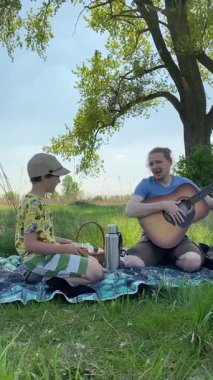 Genç bir baba ve oğlunun yaz pikniğini otlakta birlikte geçirdiği dikey görüntüler. Dışarıdaki eğlenceli aktivitelere katılıyorlar, sıcak güneşin altında mutlu anılar yaratıyorlar.