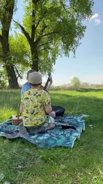 Genç bir baba ve oğlunun yaz pikniğini otlakta birlikte geçirdiği dikey görüntüler. Dışarıdaki eğlenceli aktivitelere katılıyorlar, sıcak güneşin altında mutlu anılar yaratıyorlar.