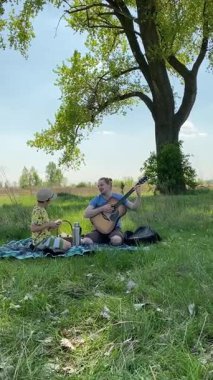 Genç bir baba ve oğlunun yaz pikniğini otlakta birlikte geçirdiği dikey görüntüler. Dışarıdaki eğlenceli aktivitelere katılıyorlar, sıcak güneşin altında mutlu anılar yaratıyorlar.