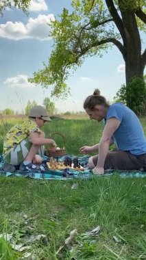 Genç bir baba ve oğlunun yaz pikniğini otlakta birlikte geçirdiği dikey görüntüler. Dışarıdaki eğlenceli aktivitelere katılıyorlar, sıcak güneşin altında mutlu anılar yaratıyorlar.