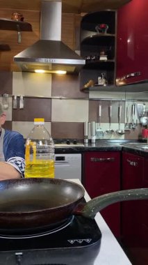 Modern bir ev mutfağında yemek hazırlayan önlüklü yaşlı bir kadının dikey hali. İçeriğiyle dikkatlice ilgilenir, ev ortamında deneyimli bir şekilde yemek pişirme sürecine odaklanır.