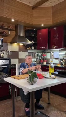 Modern bir ev mutfağında yemek hazırlayan önlüklü yaşlı bir kadının dikey hali. İçeriğiyle dikkatlice ilgilenir, ev ortamında deneyimli bir şekilde yemek pişirme sürecine odaklanır.