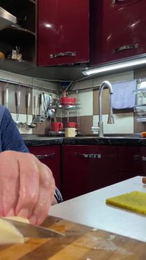 Modern bir ev mutfağında yemek hazırlayan önlüklü yaşlı bir kadının dikey hali. İçeriğiyle dikkatlice ilgilenir, ev ortamında deneyimli bir şekilde yemek pişirme sürecine odaklanır.