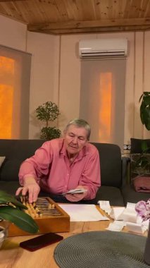 Oturma odasında vergileri, elektrik faturalarını akıllı telefon ve abaküs kullanarak hesap yapan yaşlı bir kadın. Odaklanmış ve düşünceli. Ekonomisini hem modern hem de geleneksel araçlarla yönetiyor.