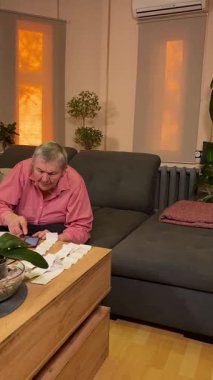 Oturma odasında vergileri, elektrik faturalarını akıllı telefon ve abaküs kullanarak hesap yapan yaşlı bir kadın. Odaklanmış ve düşünceli. Ekonomisini hem modern hem de geleneksel araçlarla yönetiyor.