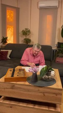 Oturma odasında vergileri, elektrik faturalarını akıllı telefon ve abaküs kullanarak hesap yapan yaşlı bir kadın. Odaklanmış ve düşünceli. Ekonomisini hem modern hem de geleneksel araçlarla yönetiyor.