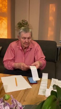 Oturma odasında vergileri, elektrik faturalarını akıllı telefon ve abaküs kullanarak hesap yapan yaşlı bir kadın. Odaklanmış ve düşünceli. Ekonomisini hem modern hem de geleneksel araçlarla yönetiyor.