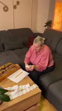 Oturma odasında vergileri, elektrik faturalarını akıllı telefon ve abaküs kullanarak hesap yapan yaşlı bir kadın. Odaklanmış ve düşünceli. Ekonomisini hem modern hem de geleneksel araçlarla yönetiyor.