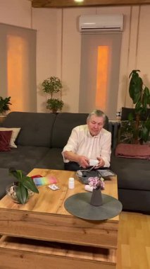 Sıcaklığı, oturma odasındaki kan basıncını ölçerek sağlıkla ilgilenen dikey yaşlı kadın. Günlük ilaç organizatörü ve ilaç çevrede görünüyor, rutin ve tıbbi bakımını yansıtıyor.