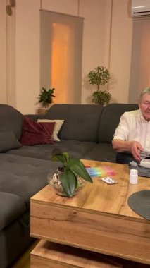 Sıcaklığı, oturma odasındaki kan basıncını ölçerek sağlıkla ilgilenen dikey yaşlı kadın. Günlük ilaç organizatörü ve ilaç çevrede görünüyor, rutin ve tıbbi bakımını yansıtıyor.