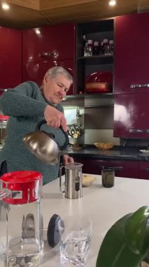 Dikey yaşlı kadın sıcak bir ev mutfağında öğle yemeği yiyor, sıcak bir ev yemeği yiyor. Yavaş ve dikkatli bir şekilde yiyor, tanıdık yiyeceklerin rahatlığını ve etrafındaki sakin atmosferi takdir ediyor.. 