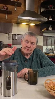 Dikey yaşlı kadın sıcak bir ev mutfağında öğle yemeği yiyor, sıcak bir ev yemeği yiyor. Yavaş ve dikkatli bir şekilde yiyor, tanıdık yiyeceklerin rahatlığını ve etrafındaki sakin atmosferi takdir ediyor.. 