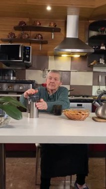 Dikey yaşlı kadın sıcak bir ev mutfağında öğle yemeği yiyor, sıcak bir ev yemeği yiyor. Yavaş ve dikkatli bir şekilde yiyor, tanıdık yiyeceklerin rahatlığını ve etrafındaki sakin atmosferi takdir ediyor.. 