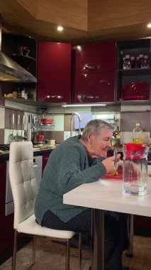 Dikey yaşlı kadın sıcak bir ev mutfağında öğle yemeği yiyor, sıcak bir ev yemeği yiyor. Yavaş ve dikkatli bir şekilde yiyor, tanıdık yiyeceklerin rahatlığını ve etrafındaki sakin atmosferi takdir ediyor.. 