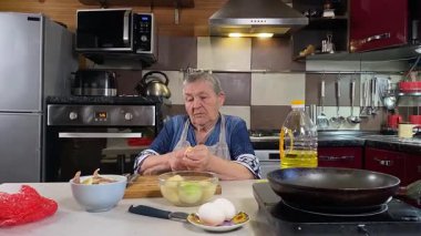 Modern bir ev mutfağında yemek hazırlayan kısa gri saçlı yaşlı bir kadın. İçeriğiyle dikkatlice ilgilenir, ev ortamında deneyimli bir şekilde yemek pişirme sürecine odaklanır. 