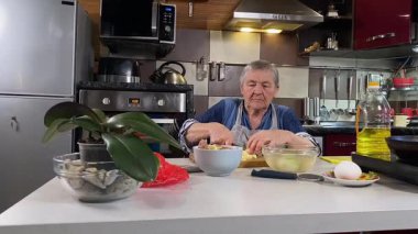 Modern bir ev mutfağında yemek hazırlayan kısa gri saçlı yaşlı bir kadın. İçeriğiyle dikkatlice ilgilenir, ev ortamında deneyimli bir şekilde yemek pişirme sürecine odaklanır. 