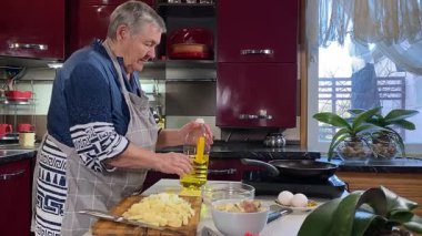 Modern bir ev mutfağında yemek hazırlayan kısa gri saçlı yaşlı bir kadın. İçeriğiyle dikkatlice ilgilenir, ev ortamında deneyimli bir şekilde yemek pişirme sürecine odaklanır. 