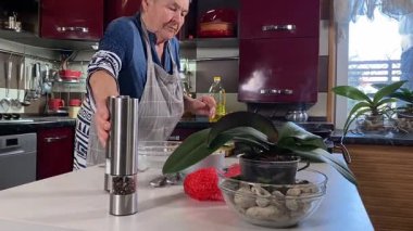 Modern bir ev mutfağında yemek hazırlayan kısa gri saçlı yaşlı bir kadın. İçeriğiyle dikkatlice ilgilenir, ev ortamında deneyimli bir şekilde yemek pişirme sürecine odaklanır. 