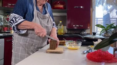 Modern bir ev mutfağında yemek hazırlayan kısa gri saçlı yaşlı bir kadın. İçeriğiyle dikkatlice ilgilenir, ev ortamında deneyimli bir şekilde yemek pişirme sürecine odaklanır. 