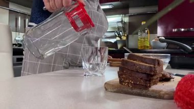 Modern bir ev mutfağında yemek hazırlayan kısa gri saçlı yaşlı bir kadın. İçeriğiyle dikkatlice ilgilenir, ev ortamında deneyimli bir şekilde yemek pişirme sürecine odaklanır. 