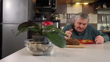 Sıcak bir ev mutfağında öğle yemeği yiyen, ev yapımı sıcak yemeğin tadını çıkaran yaşlı bir kadın. Yavaş ve dikkatli bir şekilde yiyor, tanıdık yiyeceklerin rahatlığını ve etrafındaki sakin atmosferi takdir ediyor.. 