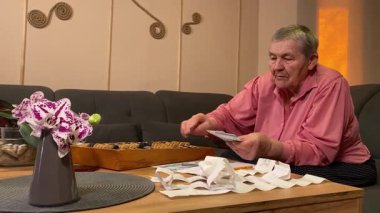 Oturma odasında vergileri, elektrik faturalarını akıllı telefon ve abaküs kullanarak hesap yapan yaşlı bir kadın. Odaklanmış ve düşünceli. Ekonomisini hem modern hem de geleneksel araçlarla yönetiyor. 