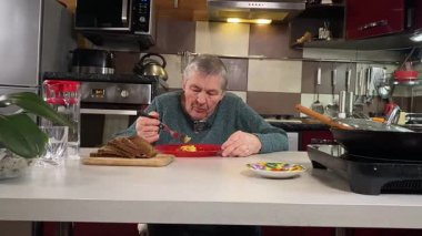 Sıcak bir ev mutfağında öğle yemeği yiyen, ev yapımı sıcak yemeğin tadını çıkaran yaşlı bir kadın. Yavaş ve dikkatli bir şekilde yiyor, tanıdık yiyeceklerin rahatlığını ve etrafındaki sakin atmosferi takdir ediyor.. 