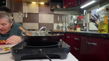 Sıcak bir ev mutfağında öğle yemeği yiyen, ev yapımı sıcak yemeğin tadını çıkaran yaşlı bir kadın. Yavaş ve dikkatli bir şekilde yiyor, tanıdık yiyeceklerin rahatlığını ve etrafındaki sakin atmosferi takdir ediyor.. 