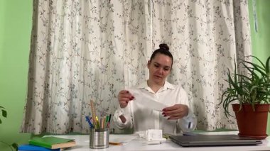 İş elbiseli genç bir kadın ev ofisinde çalışıyor, dizüstü bilgisayar ve telefon kullanıyor. Odaklanmış ve profesyonel olarak, günlük rutininde teknoloji ve iletişimi birleştirerek görevleri etkili bir şekilde yönetiyor. 