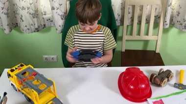 İlkokul çağındaki neşeli genç bir çocuk kapalı bir masada otururken oyuncaklarla oynuyor. Enerji ve hayal gücüyle dolu, rahat, güvenli ve yaratıcı bir ortamda eğleniyor.. 