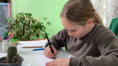 Genç kız evde yaratıcı aktiviteler yapıyor, hobisinin bir parçası olarak kalemlerle resim çiziyor. Odaklanmış ve ilham almış, sanatsal ifadenin günümüze getirdiği eğlence ve rahatlıktan zevk alıyor.. 