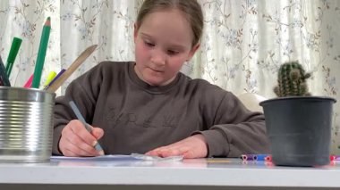 Genç kız evde yaratıcı aktiviteler yapıyor, hobisinin bir parçası olarak kalemlerle resim çiziyor. Odaklanmış ve ilham almış, sanatsal ifadenin günümüze getirdiği eğlence ve rahatlıktan zevk alıyor.. 